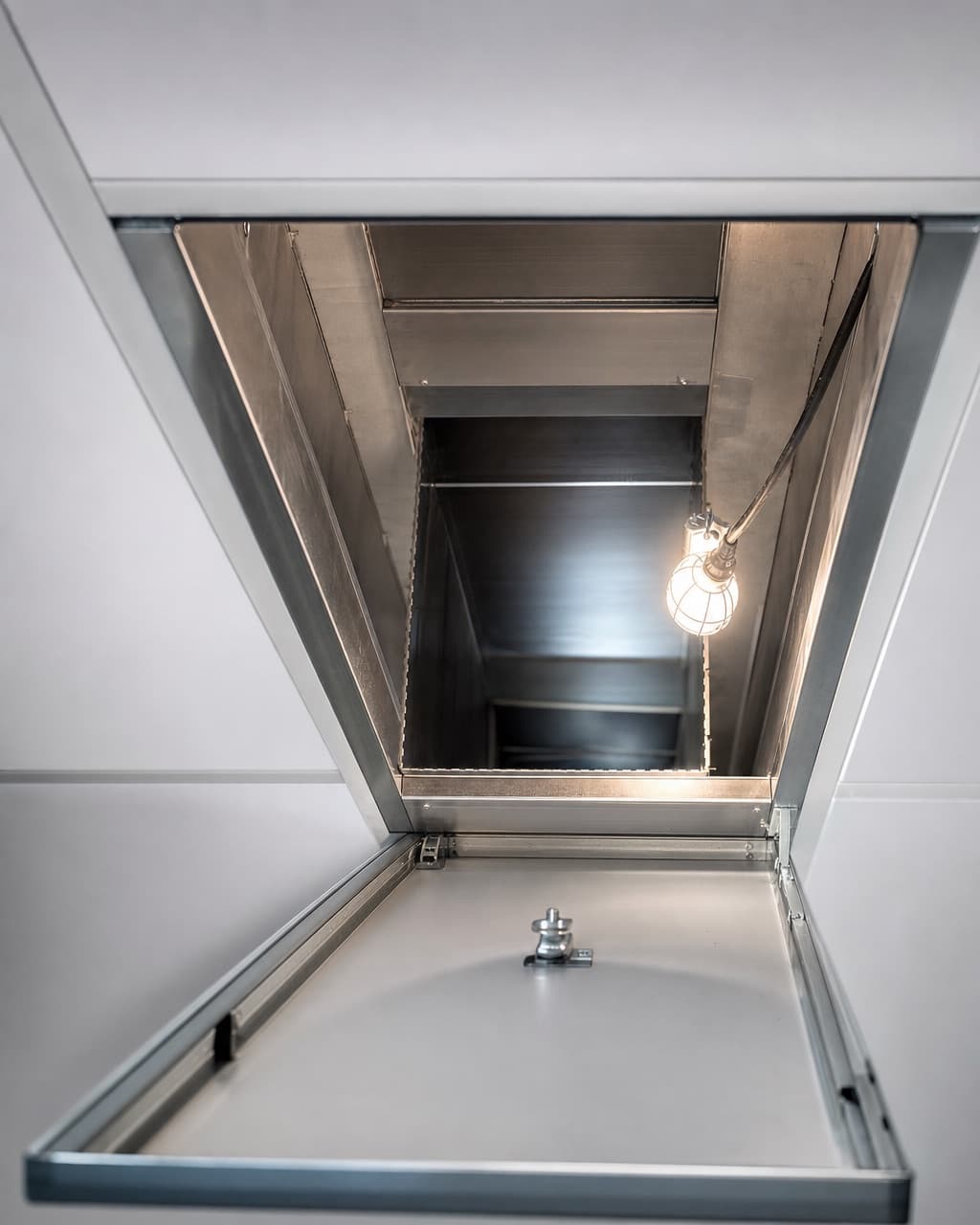 Un conduit d’extraction rectangulaire en inox traversant un faux plafond, une trappe de visite ouverte